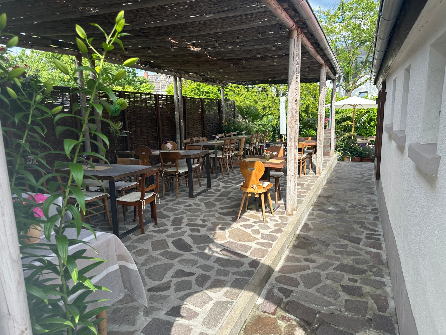 Überdachte Terrasse mit Holzpfosten, Natursteinboden und gedeckten Tischen