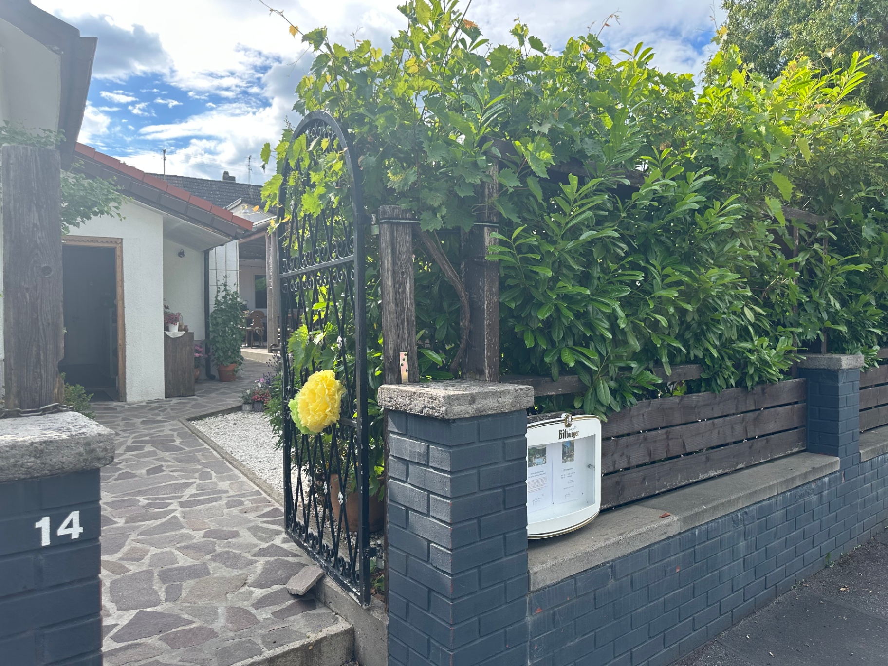 Eingang des Restaurants mit Tor, Weinlaub und Gartenweg.