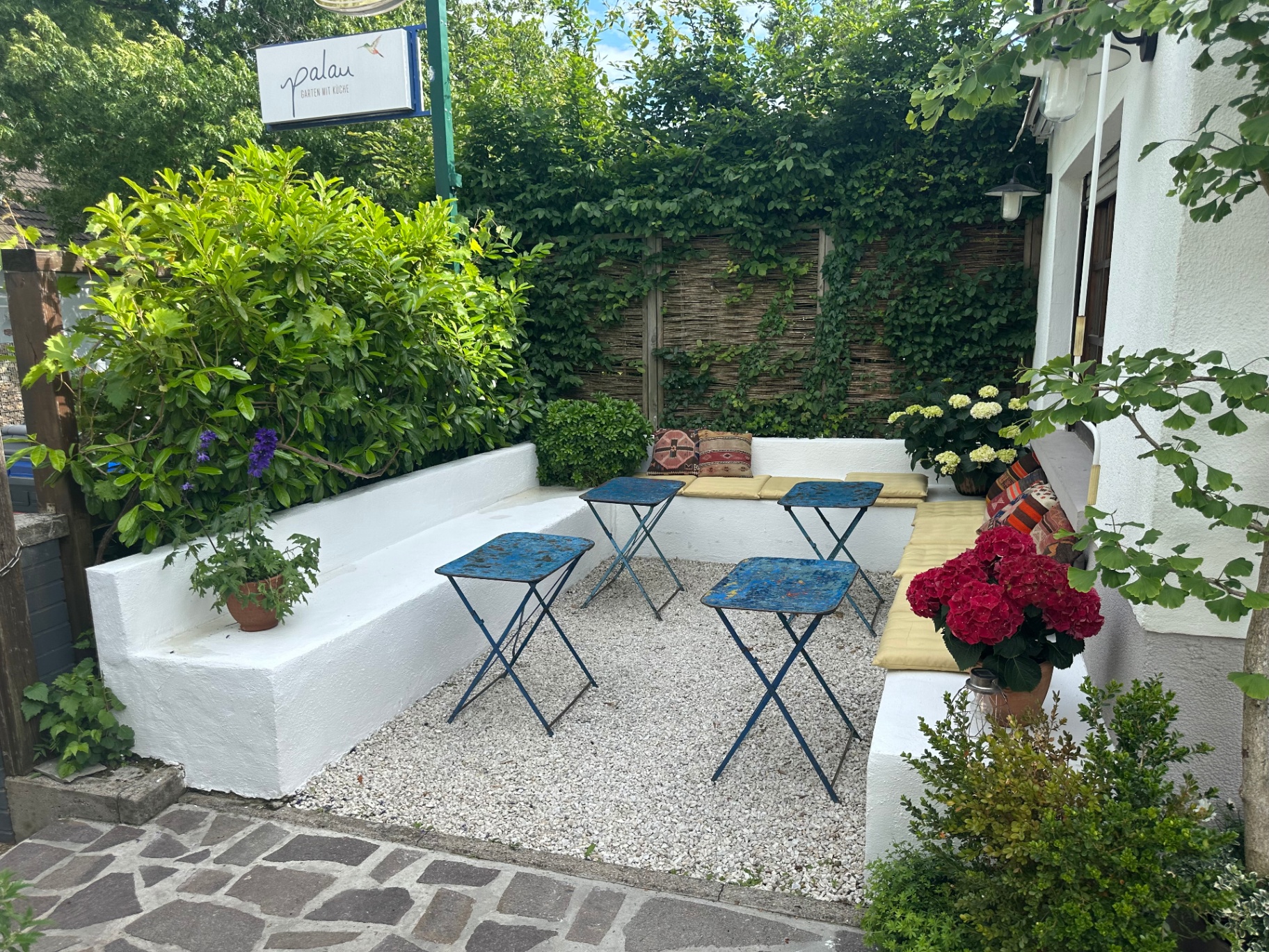 Kleiner ruhiger Gartenbereich mit Bänken und blauen Tischen